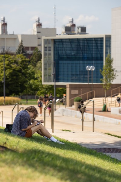 Student outside studing with campus in the background displayed in a new window